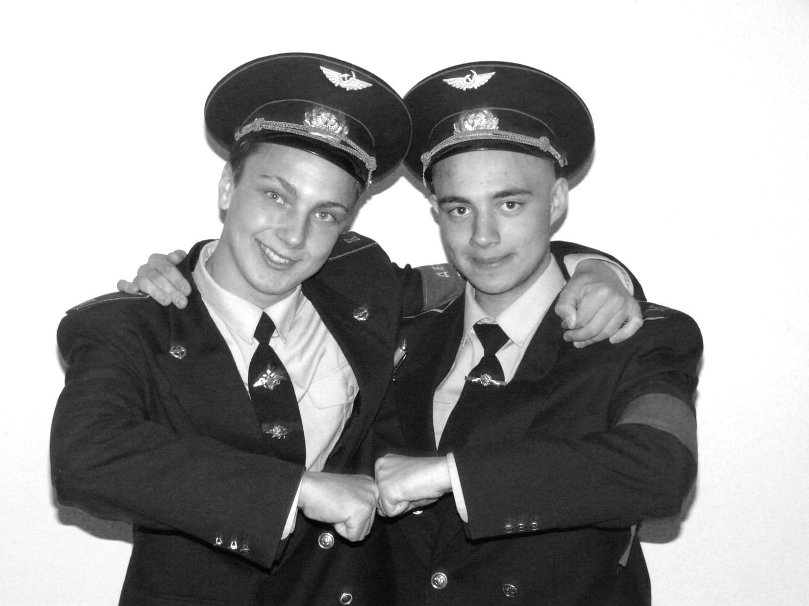 Anton Kolhonen and Pavel Zaytsev, wearing matching uniforms and caps, stand side by side with their arms around each other’s shoulders and touch fists.