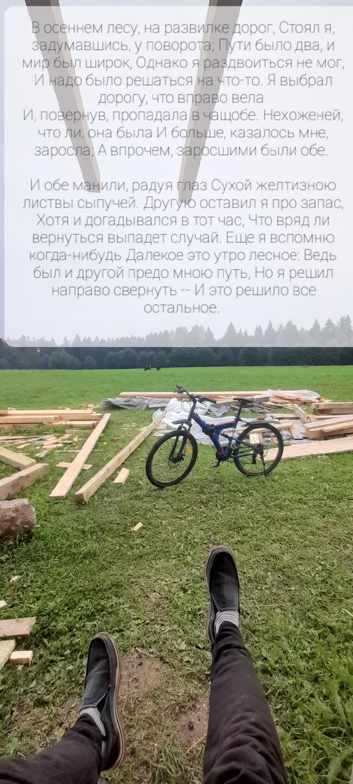 A bicycle beside a wooden house under construction, seen past a seated person’s legs, with Russian text about choosing a road overlaid above.