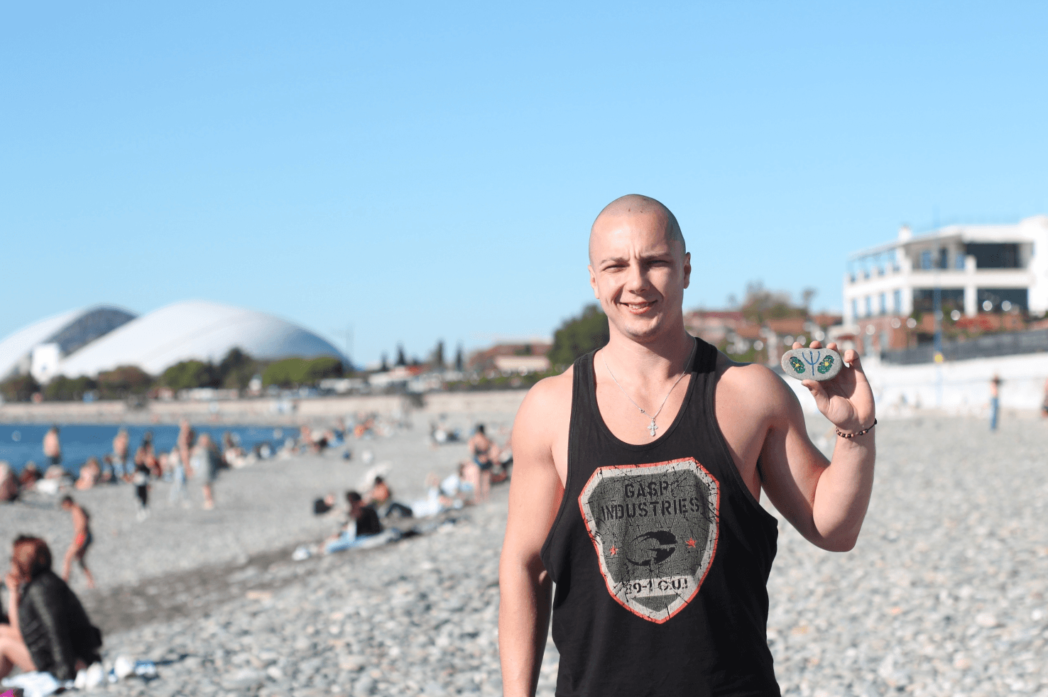 Anton Kolhonen standing on a beach in Sochi and holding two painted stones.