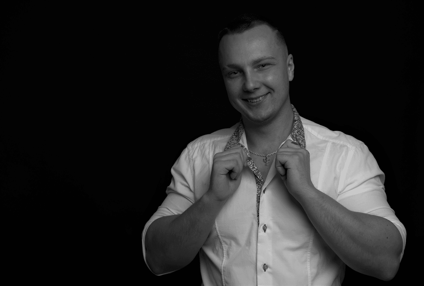 A black-and-white portrait of Anton Kolhonen smiling in a white shirt against a black background.