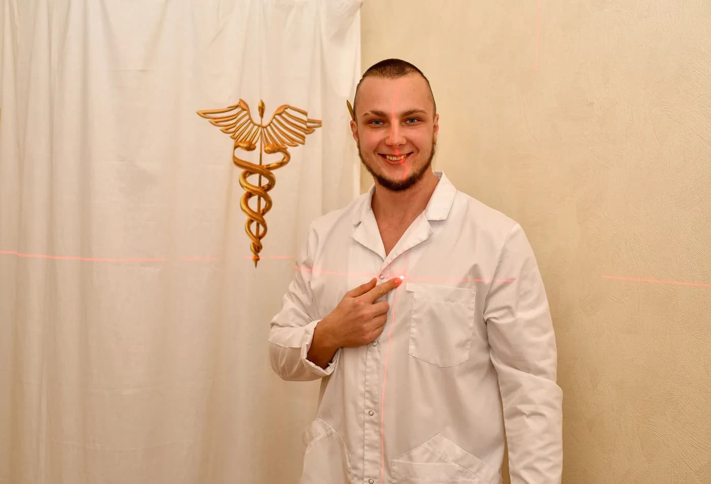Anton Kolhonen in a white coat stands beside a golden image of a caduceus.